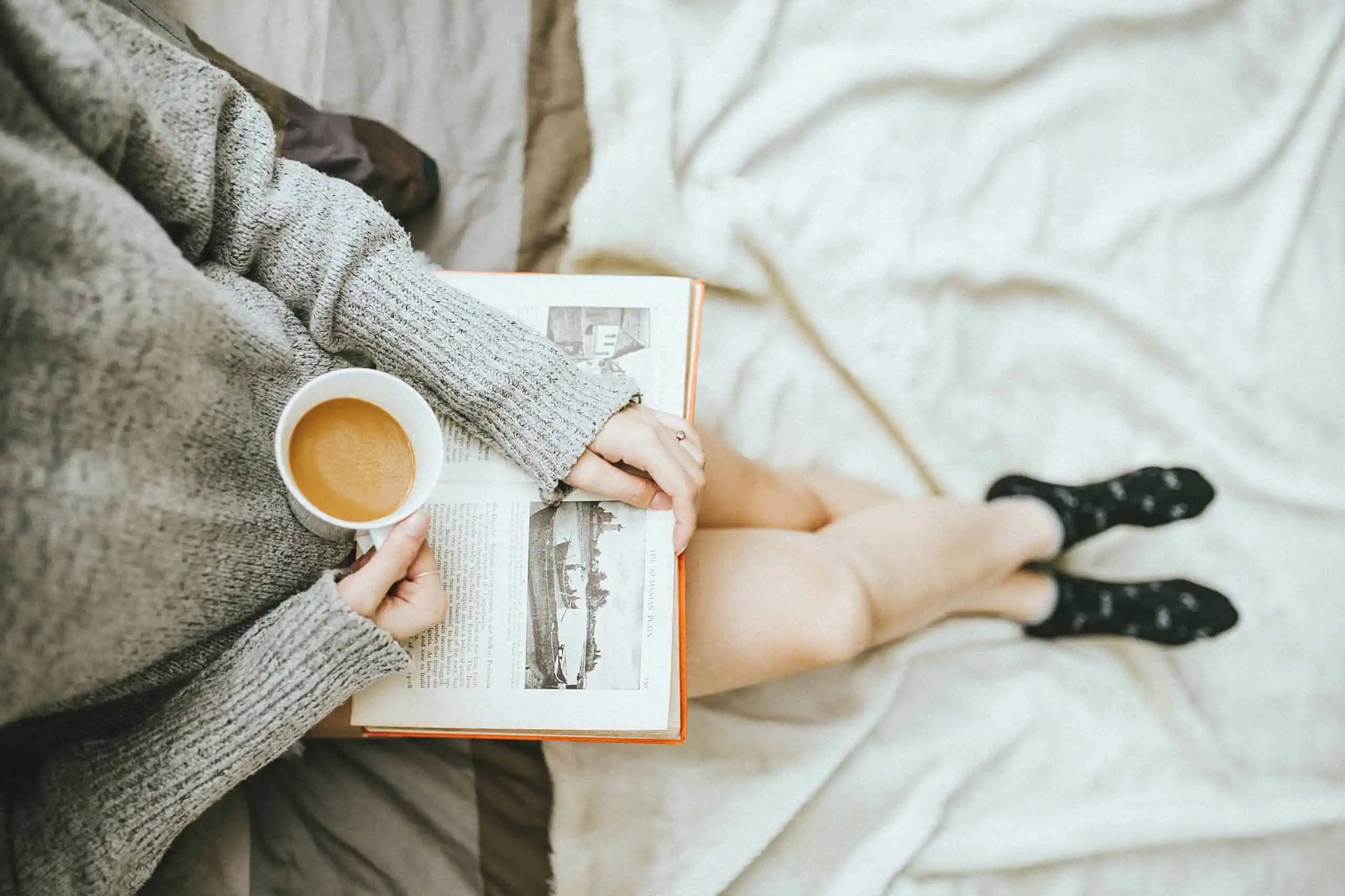 Mother reading book and holding cup of coffee